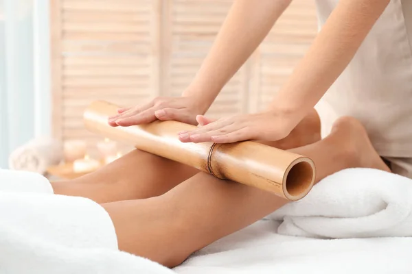 Woman having massage with bamboo stick in wellness center, closeup